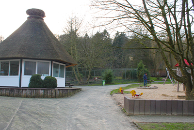 Imbiss mit Reetdach im Waldzoo, daneben Spielplatz mit Sandfläche und Wippe