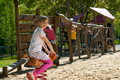 Mädchen sitzt lachend auf einer Federwippe im Spielbereich des Waldzoos