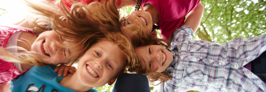 Kinder liegen im Kreis auf der Wiese und lachen in die Kamera